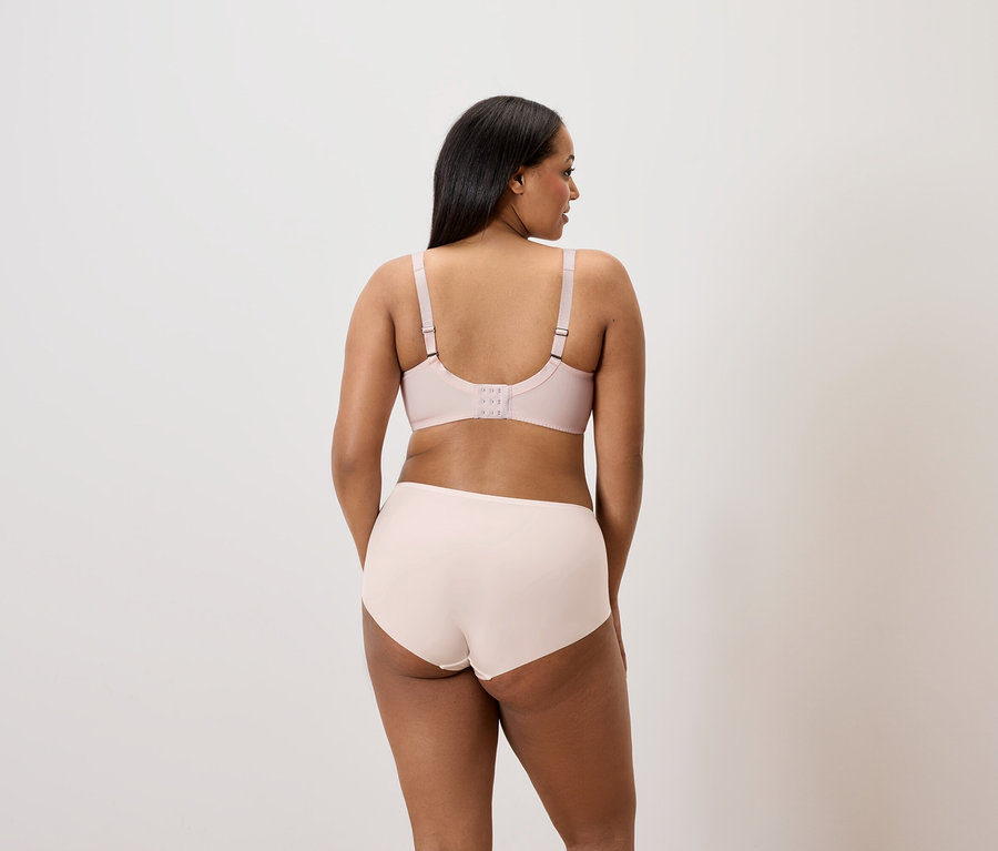 Vue arrière : une femme aux cheveux foncés porte un soutien-gorge et une culotte rose clair.