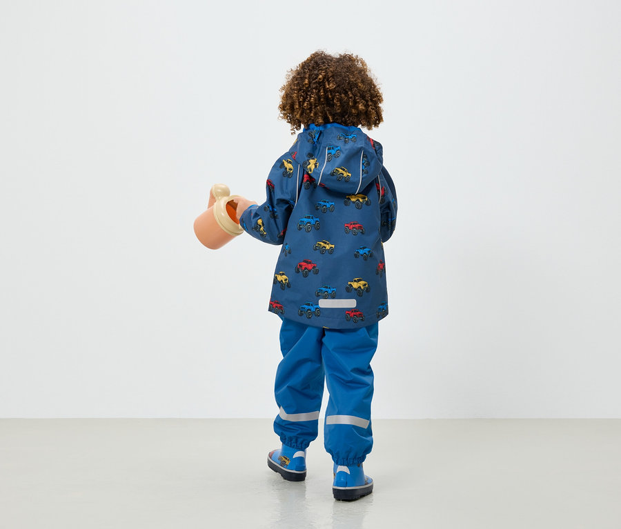 Garçon en veste et pantalon bleus avec imprimé de voitures tenant un arrosoir beige.