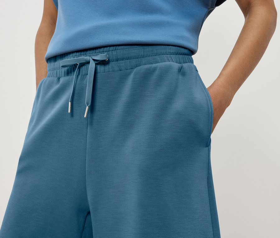 Gros plan d'une femme portant un pantalon de survêtement bleu avec une main dans la poche.