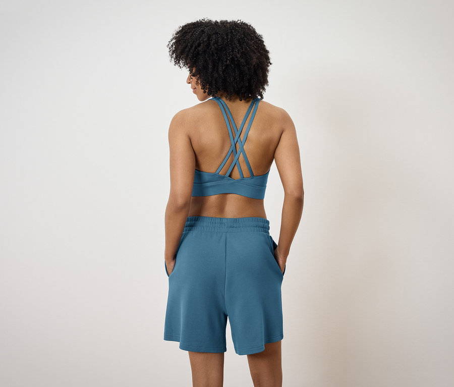 Vue arrière d'une femme afro portant un soutien-gorge de sport bleu à bretelles croisées et un short bleu.