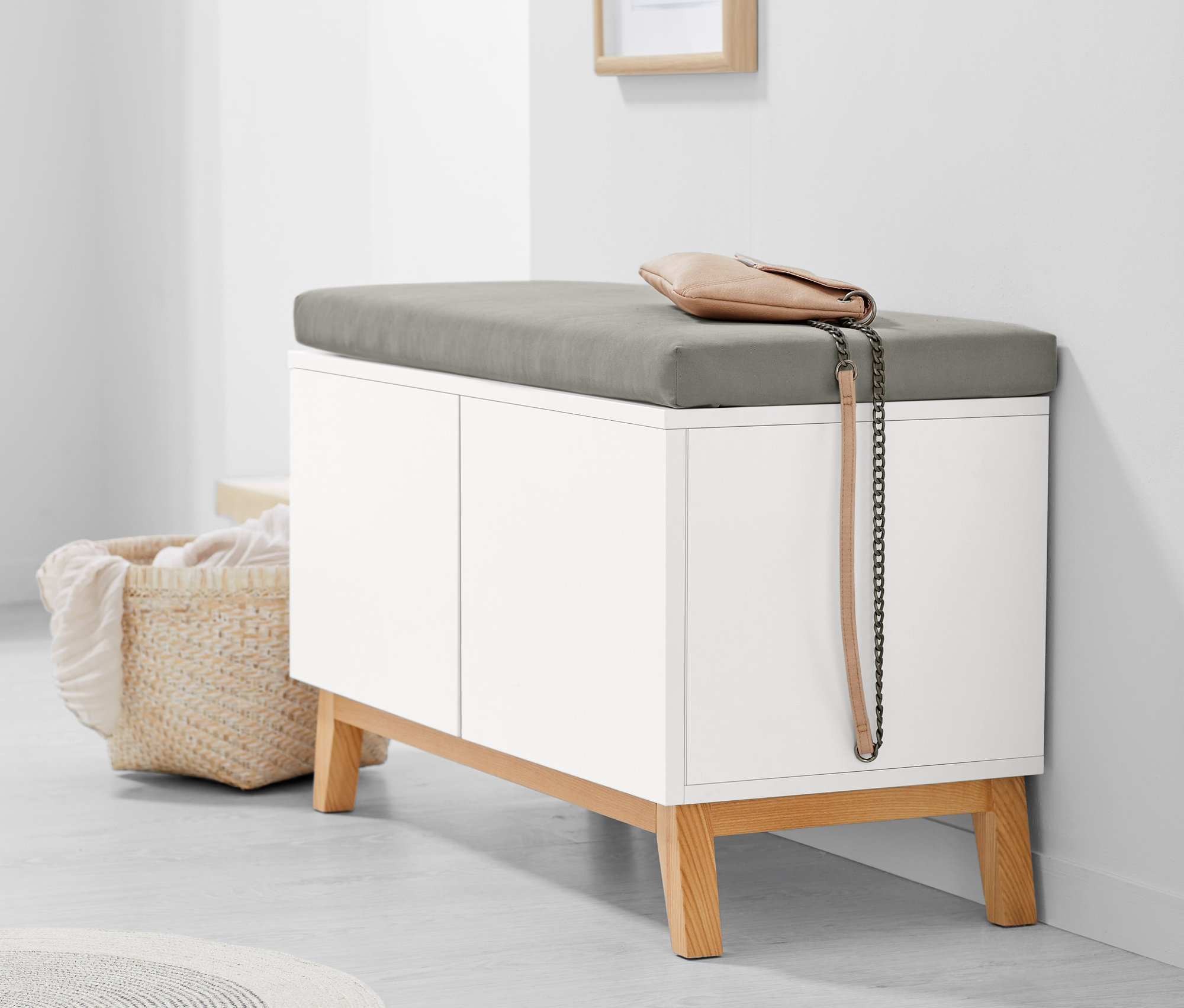 Un banc blanc avec des étagères de rangement et un coussin gris. Un sac à main beige est posé sur le banc.