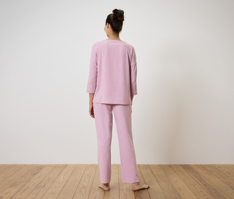 Une femme se tient dos à la caméra et porte un pyjama rose.