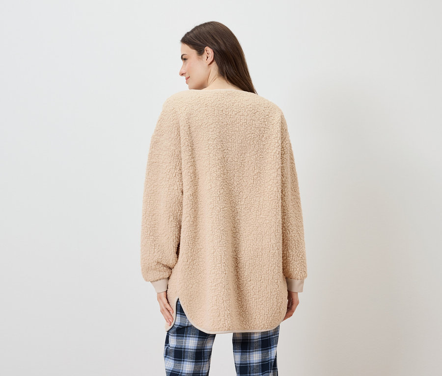 Une femme, vue de dos, porte un pull beige duveteux et un pantalon à carreaux bleus.