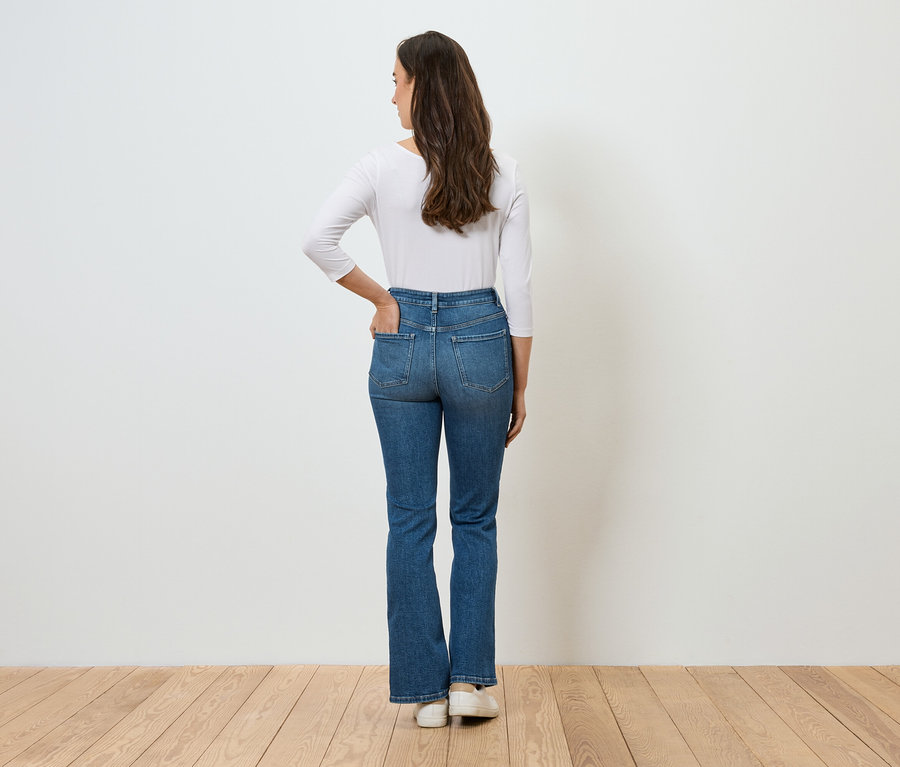 Une femme, dos à la caméra, la main dans la poche de son jean bleu et portant un t-shirt blanc à manches longues.