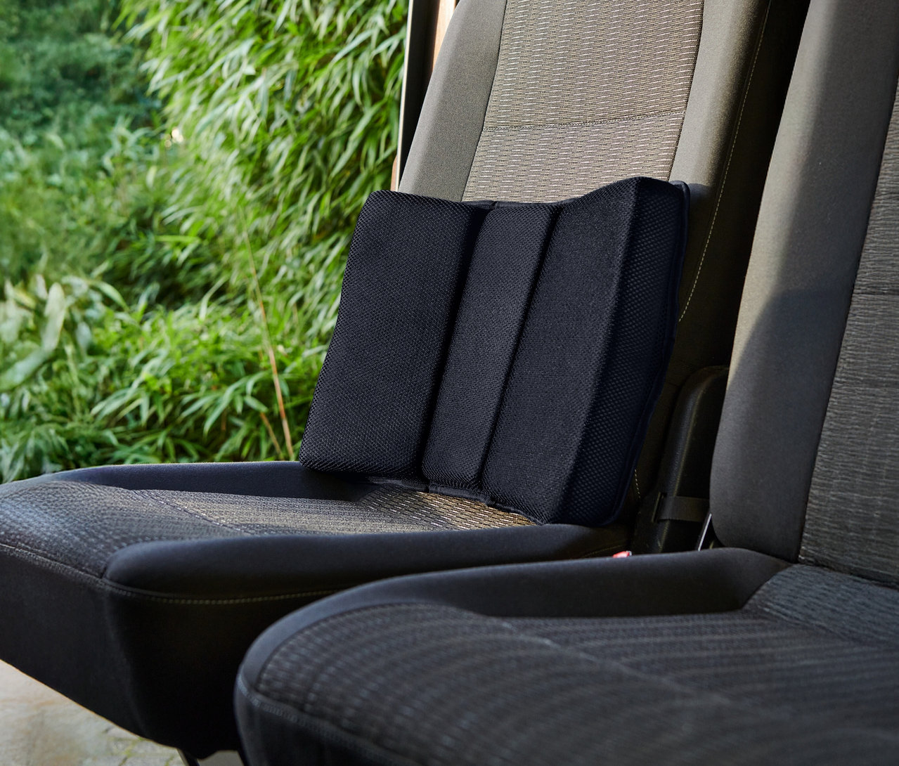 Un coussin lombaire noir est placé sur un siège de voiture.