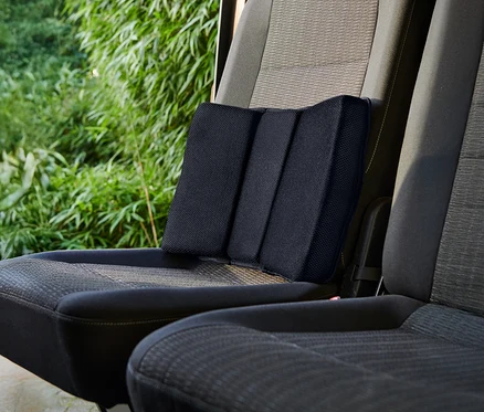 Un coussin lombaire noir est placé sur un siège de voiture.