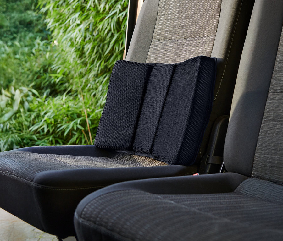Un coussin lombaire noir est placé sur un siège de voiture.