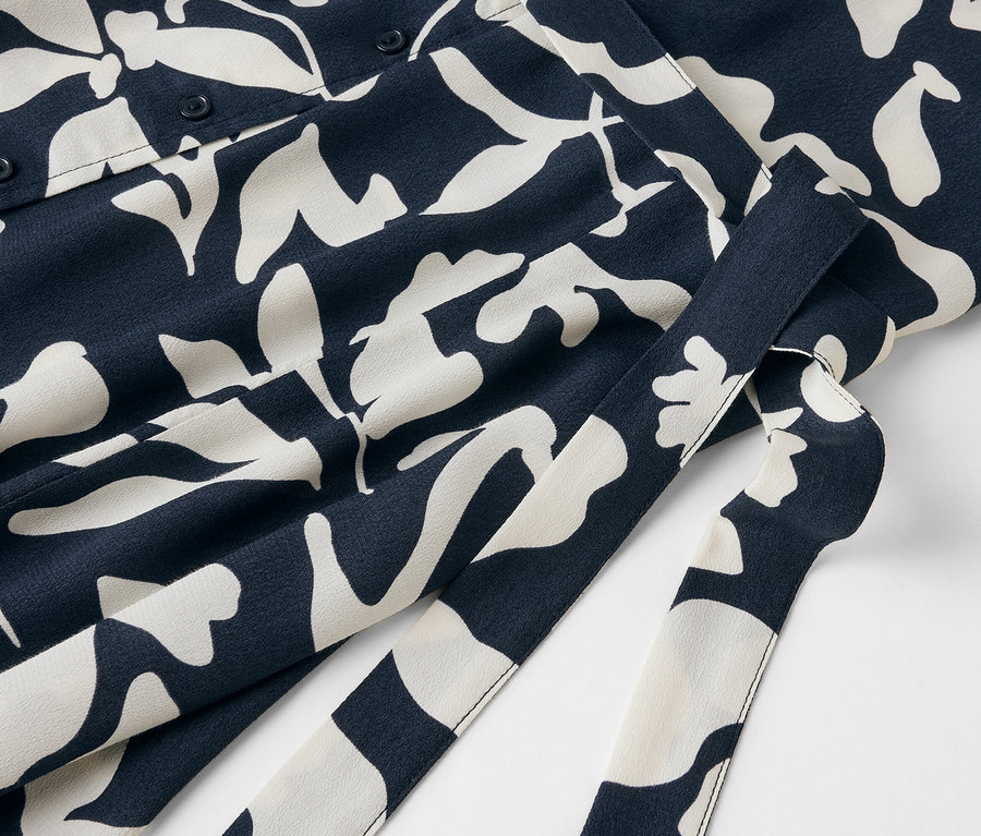 Détail d'une robe bleue avec un motif floral blanc et une ceinture.