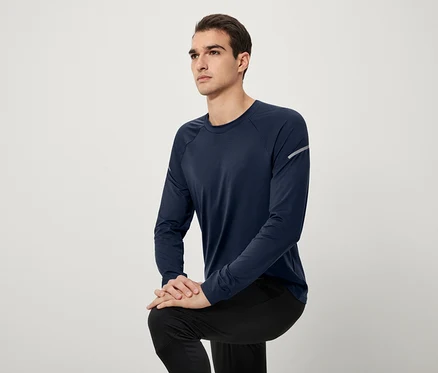 Un homme pose en t-shirt à manches longues bleu marine et pantalon noir.