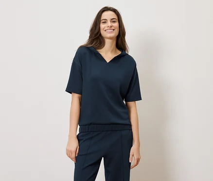 Une femme brune souriante porte un ensemble bleu marine : un haut à manches courtes et un pantalon.
