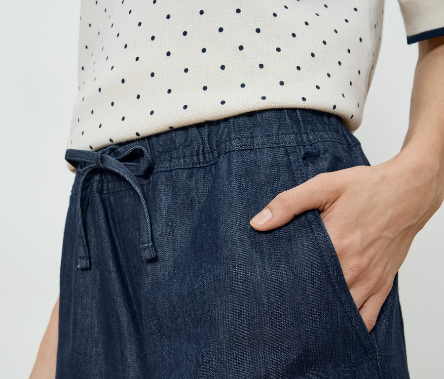 Femme avec une main dans la poche d'une jupe en jean avec cordon de serrage.