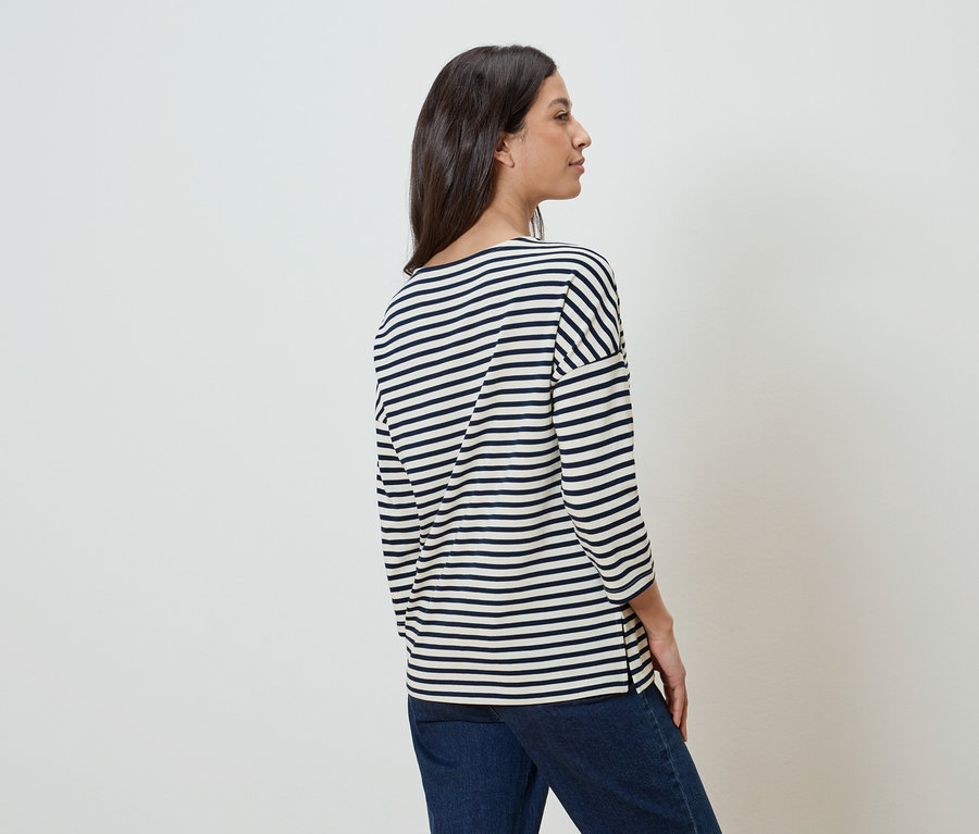 Une femme se tient de profil, portant un haut rayé et un jean.