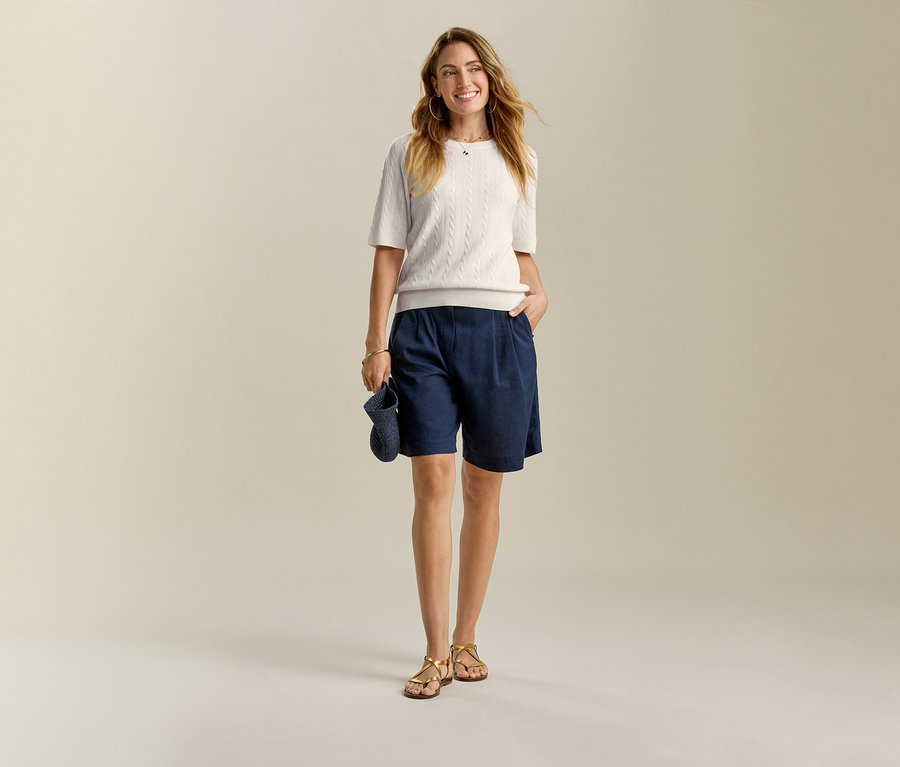 Femme portant un haut clair et un bermuda en lin bleu foncé, une main dans la poche.