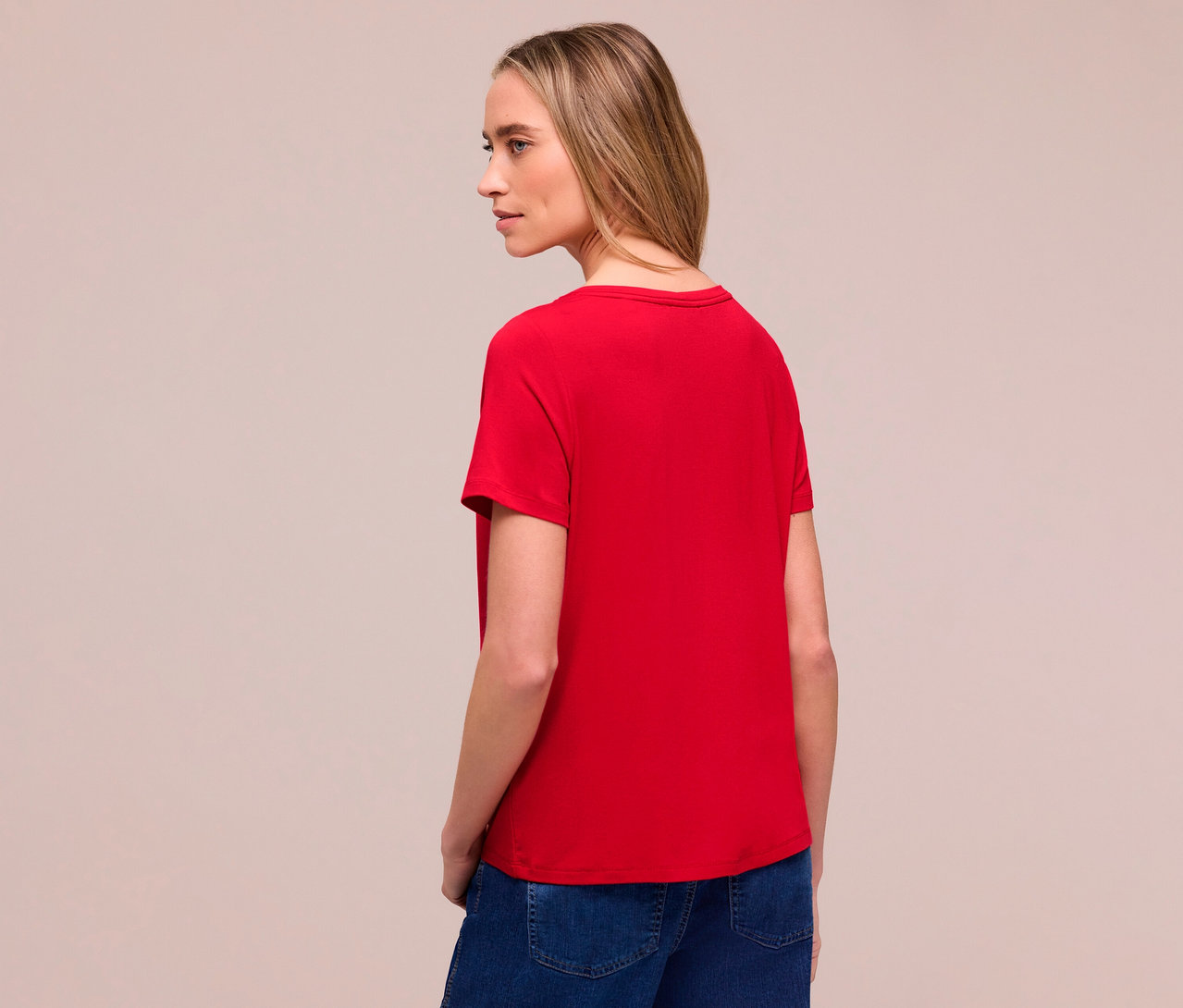 Femme de dos portant un t-shirt rouge Street One et un jean. Elle regarde vers la gauche.