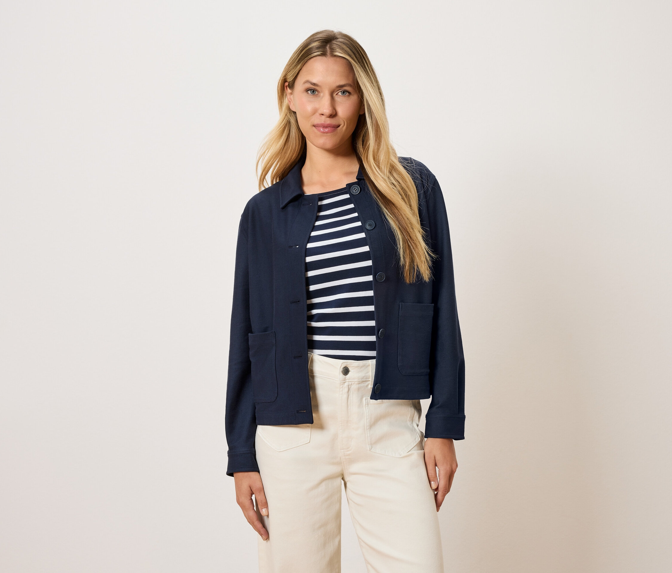 Femme portant une veste bleu marine sur un haut rayé et un pantalon crème.