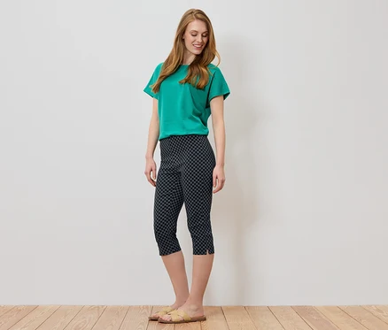 Femme aux longs cheveux roux portant un t-shirt vert et un pantacourt foncé à motifs géométriques.