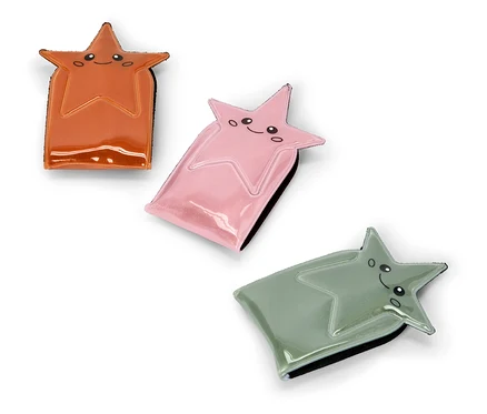 Trois pochettes brillantes en forme d'étoile, de couleur orange, rose et vert sauge, chacune avec un visage de dessin animé souriant, sont disposées en diagonale sur un fond blanc.