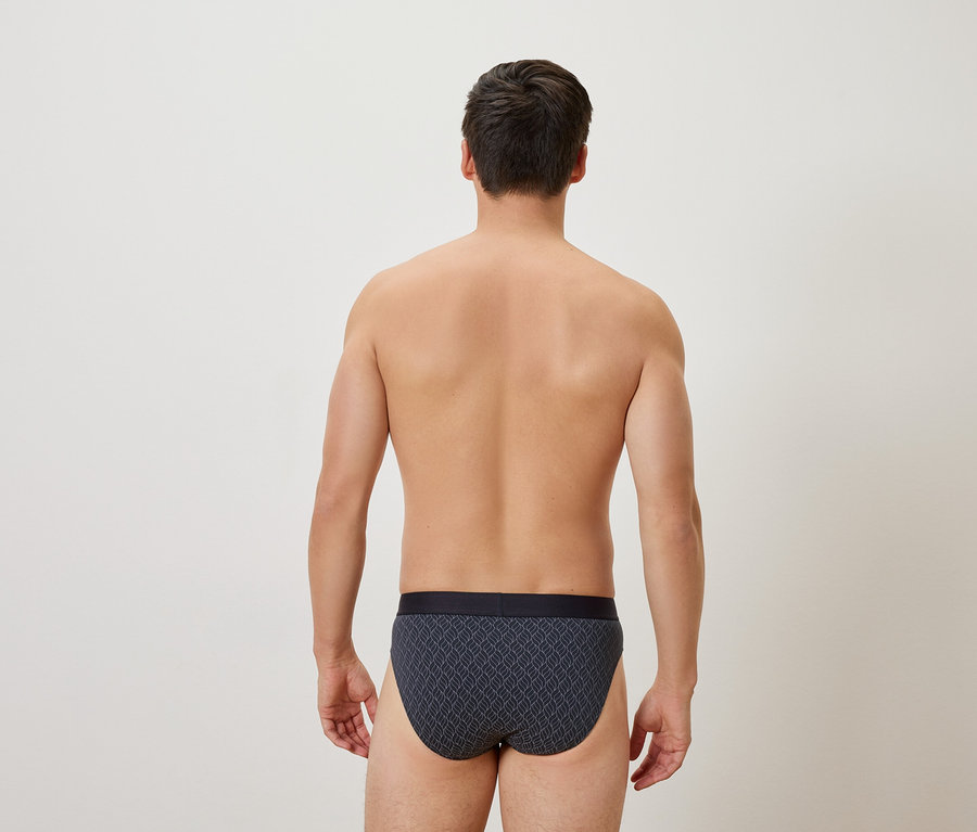 Vue arrière d'un homme portant un slip à motifs sur un fond neutre.