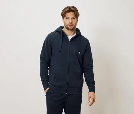 Homme portant un sweat à capuche zippé bleu marine et un pantalon de survêtement bleu marine, debout devant un fond crème.