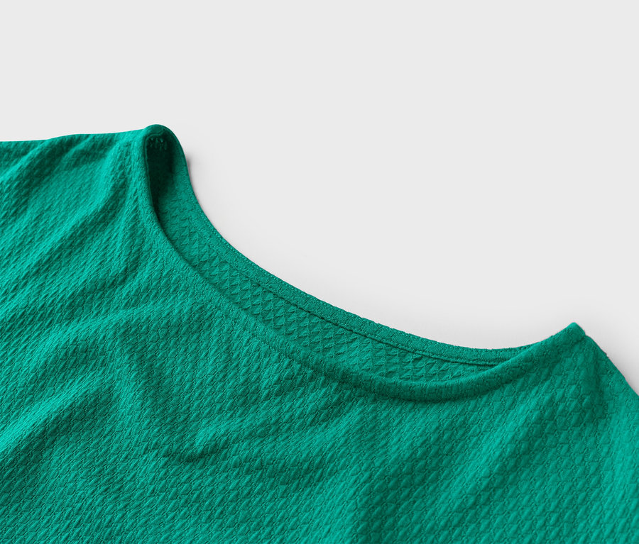 Gros plan d'un t-shirt vert émeraude à col rond avec une texture gaufrée.