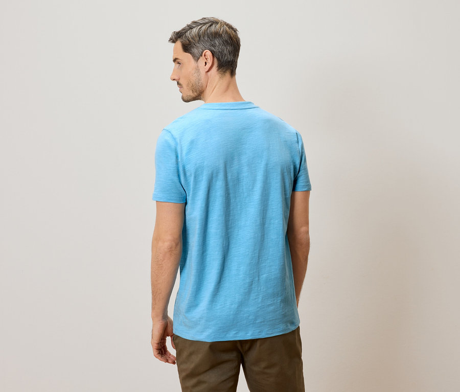 Homme vu de dos portant un t-shirt bleu clair et un pantalon marron.