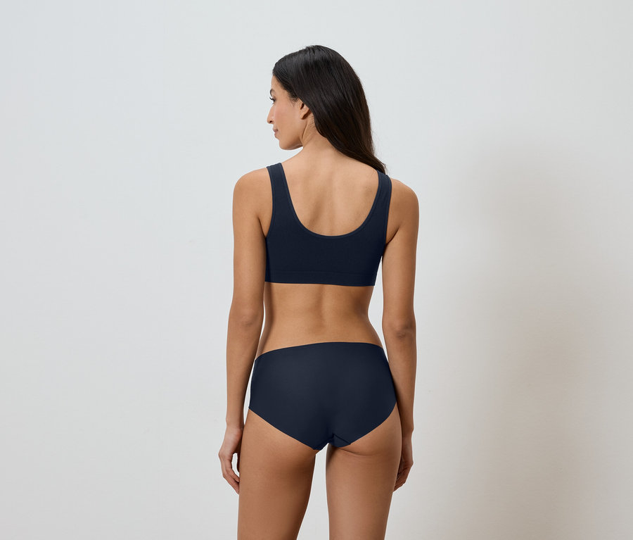 Vue de dos d'une femme aux longs cheveux foncés portant un soutien-gorge de sport bleu marine et des sous-vêtements assortis.