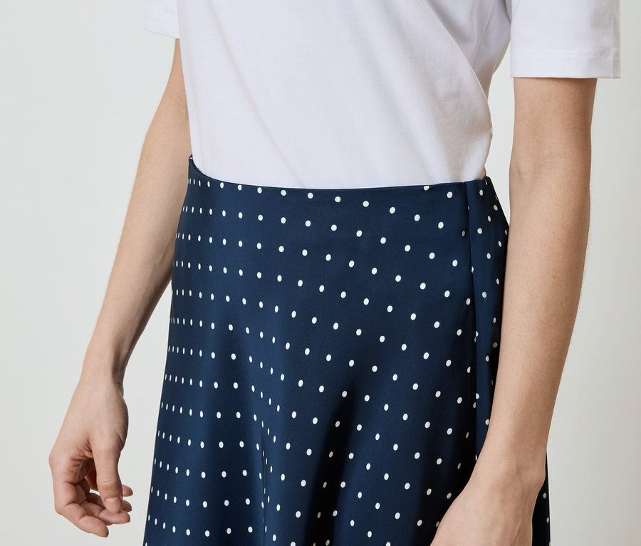 Femme portant un t-shirt blanc et une jupe bleu marine à pois blancs.