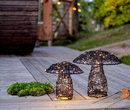 Sur une terrasse en bois, deux lampes en fil de fer noir en forme de champignon avec des lumières blanches chaudes sont posées à côté de la mousse.