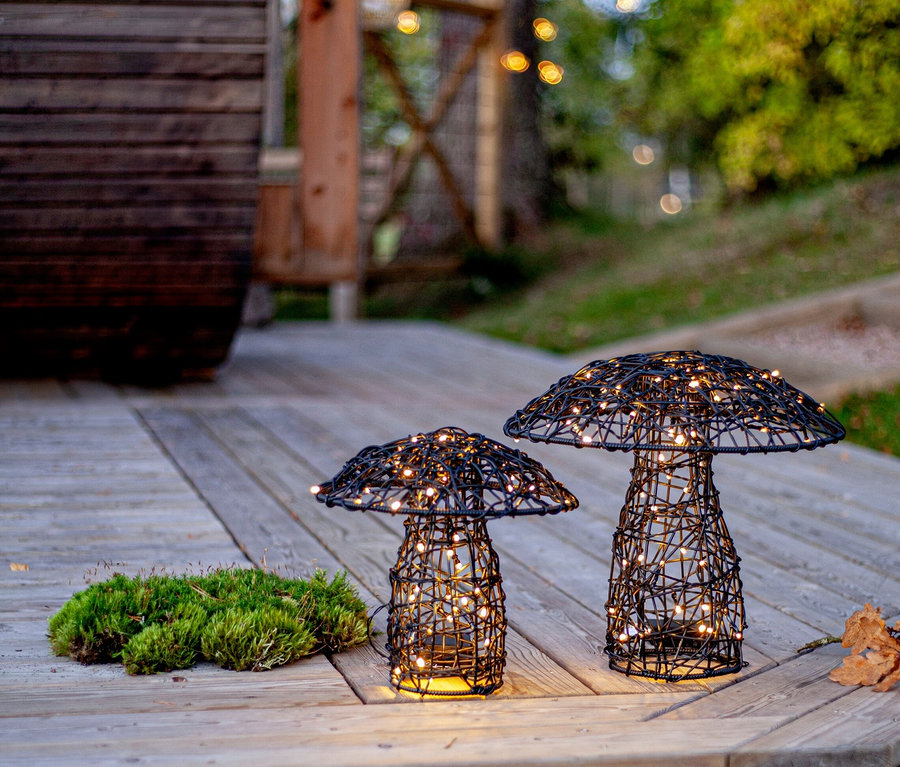 Sur une terrasse en bois, deux lampes en fil de fer noir en forme de champignon avec des lumières blanches chaudes sont posées à côté de la mousse.