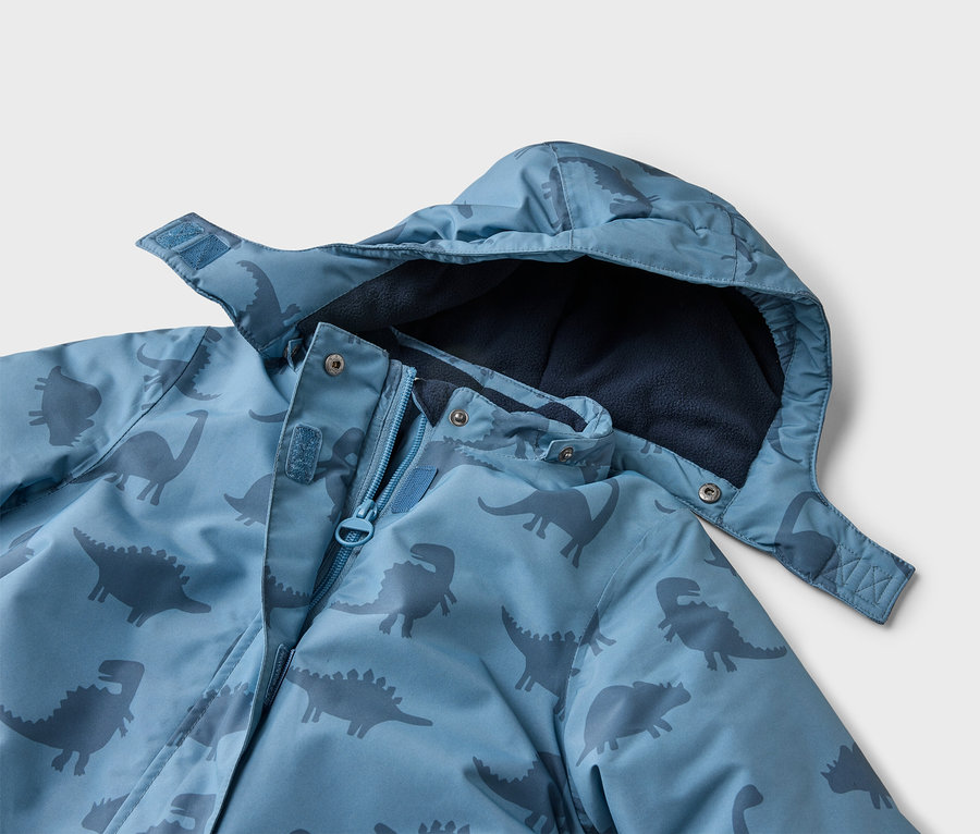 Gros plan d'une veste bleue à capuche avec motif dinosaures, partiellement ouverte, révélant une doublure en polaire bleu marine.