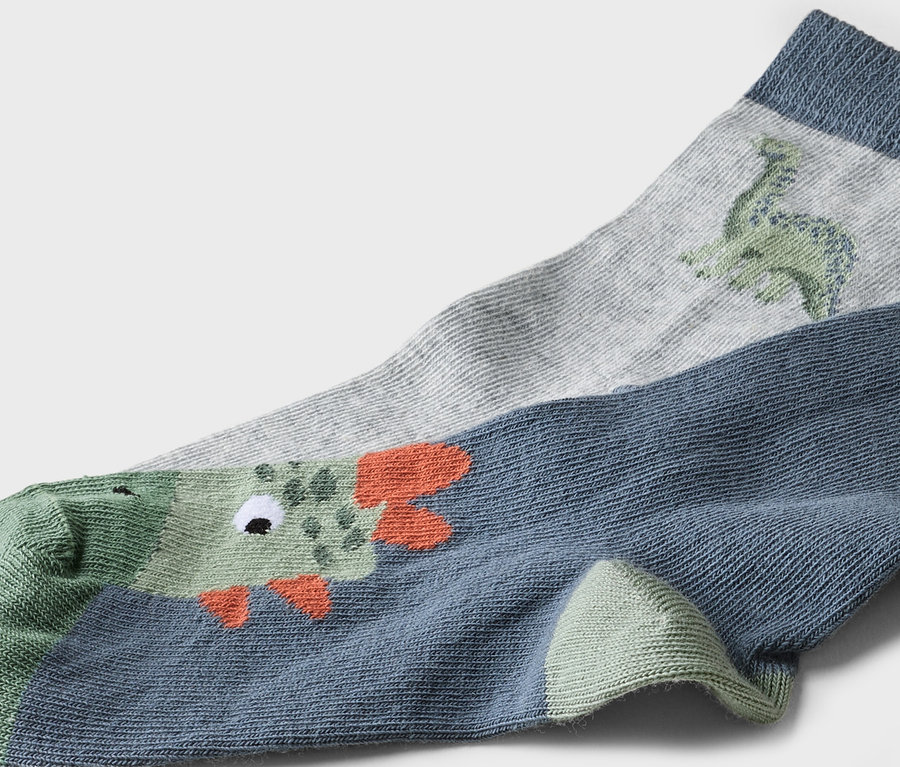 Gros plan de deux chaussettes. Une chaussette grise avec un dinosaure vert et une chaussette bleue avec un crocodile vert.