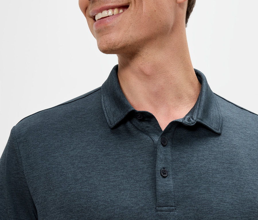 Gros plan d'un homme portant un polo bleu foncé et souriant.