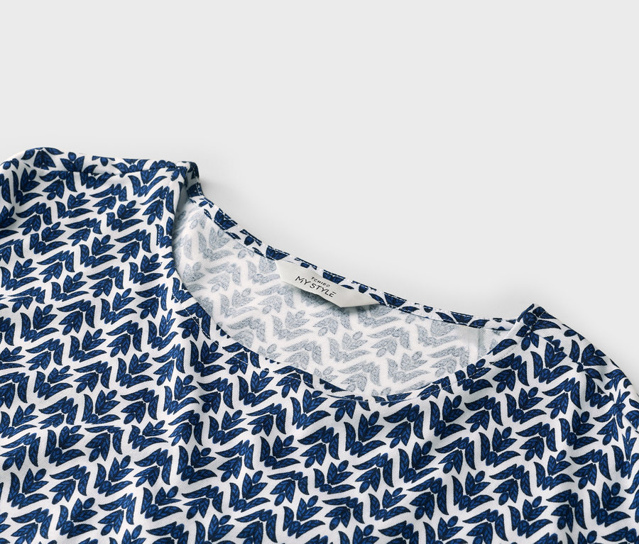 Gros plan d'un haut blanc avec un motif de feuilles bleues et une étiquette indiquant « TCHIBO MY STYLE ».