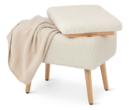 Un tabouret crème recouvert de tissu type teddy avec des pieds en bois et une couverture beige posée dessus.