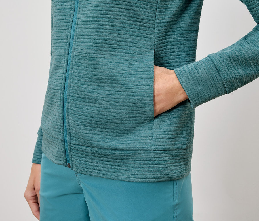 Gros plan d'une personne portant une veste et un short texturés turquoise, avec la main dans la poche de la veste.