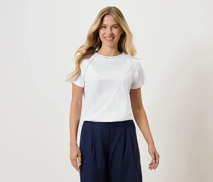 Femme portant un t-shirt blanc avec une culotte bleu marine sur un fond blanc.