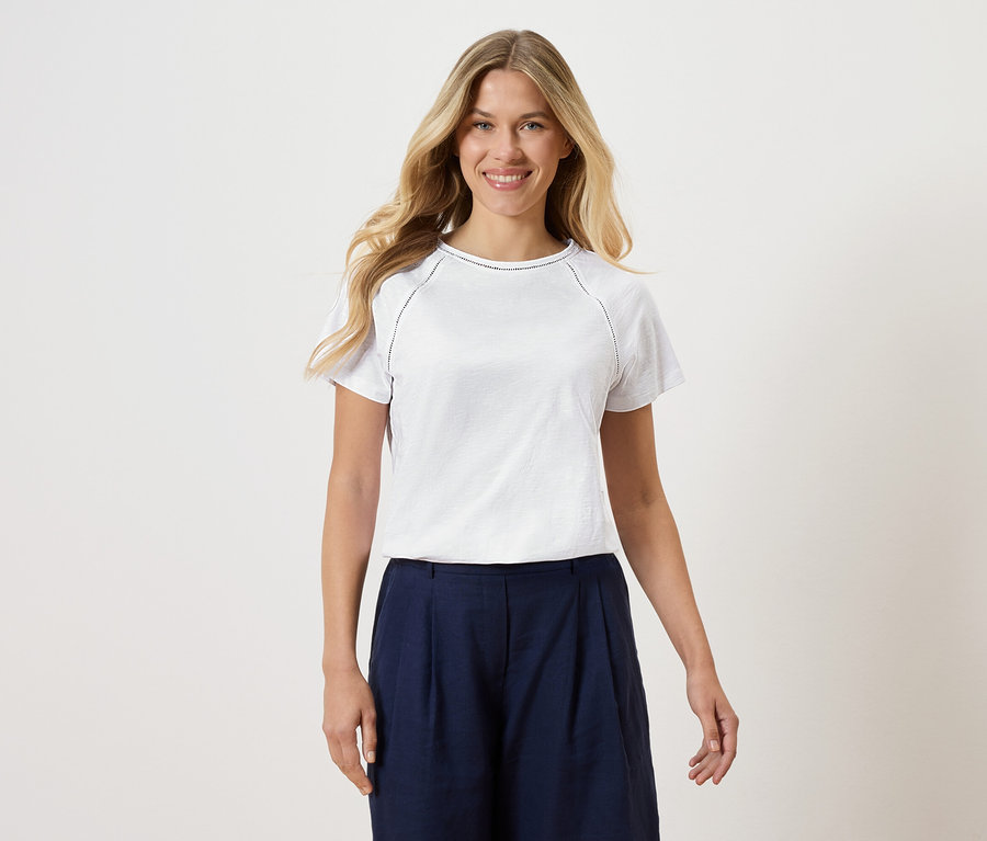 Femme portant un t-shirt blanc avec une culotte bleu marine sur un fond blanc.