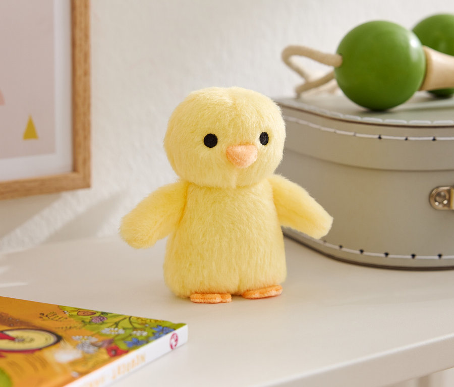 Un poussin en peluche jaune est posé sur une table à côté d'un livre, d'un cadre photo et de deux maracas.