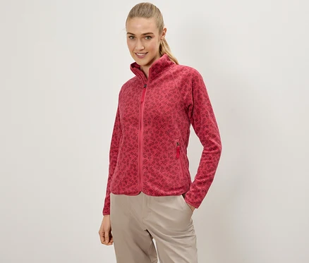 Femme posant en veste polaire rouge à fleurs et pantalon beige, une main dans la poche.