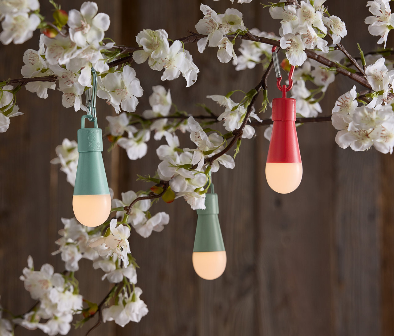 Trois lampes en forme de goutte suspendues à une branche fleurie.