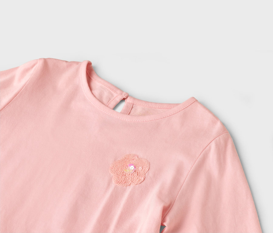 Gros plan d'une robe rose avec une fleur à paillettes sur la poitrine.
