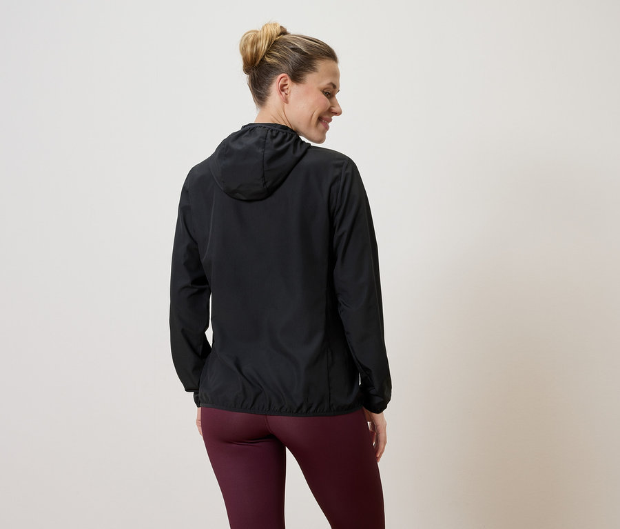Femme vue de dos portant une veste à capuche noire et un legging bordeaux sur un fond clair.
