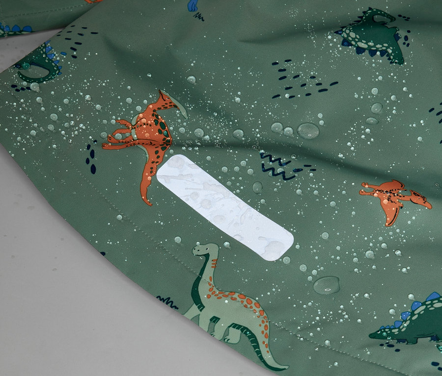 Gros plan d'un tissu vert à motif de dinosaures et gouttes d'eau, avec un patch rectangulaire réfléchissant.