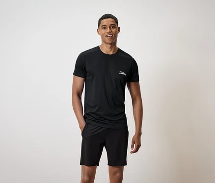 Homme portant un t-shirt noir avec un imprimé et un short noir, une main dans la poche.