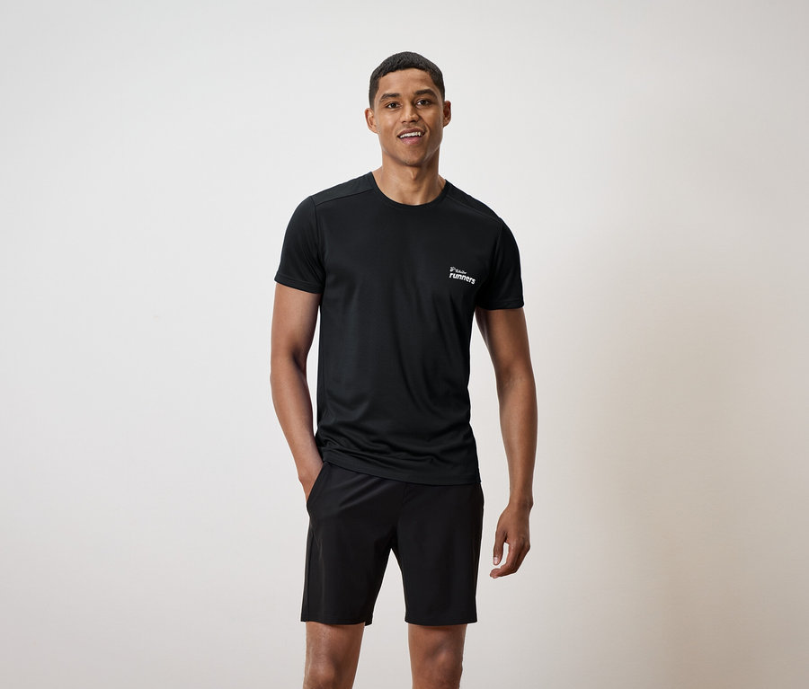 Homme portant un t-shirt noir avec un imprimé et un short noir, une main dans la poche.
