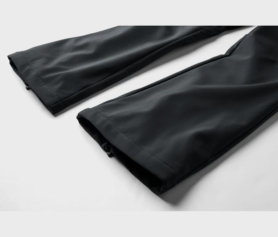 Deux jambes de pantalon noir avec des poignets zippés, posées à plat sur un fond clair.