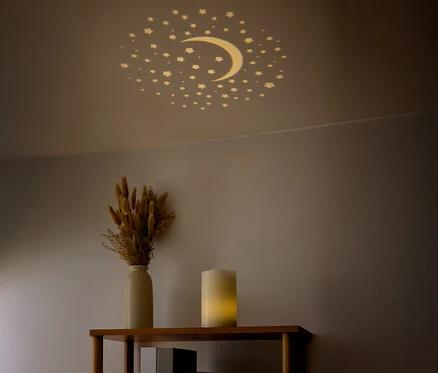Des étoiles et un croissant de lune sont visibles au plafond. Un vase avec des fleurs séchées et une bougie sont posés sur une étagère.