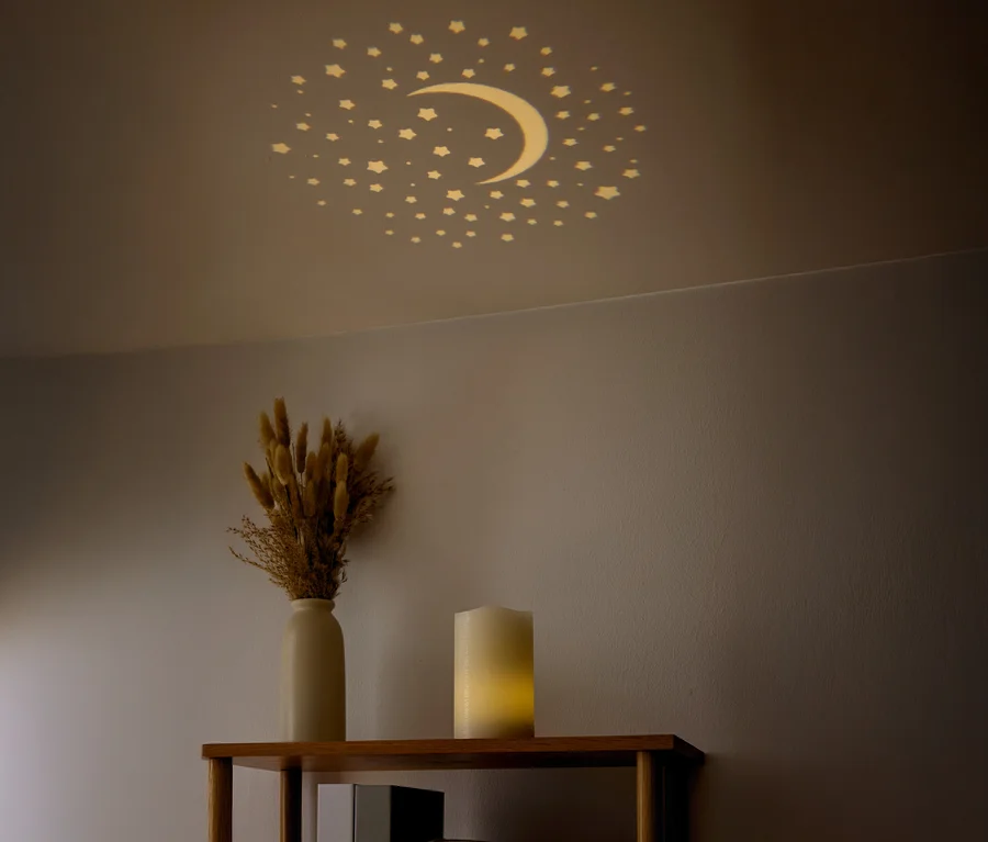 Des étoiles et un croissant de lune sont visibles au plafond. Un vase avec des fleurs séchées et une bougie sont posés sur une étagère.