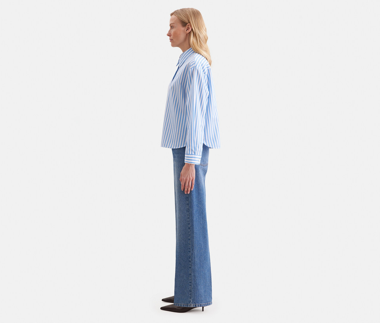 Femme de profil portant un chemisier oversize Seidensticker bleu et blanc rayé avec un jean large.