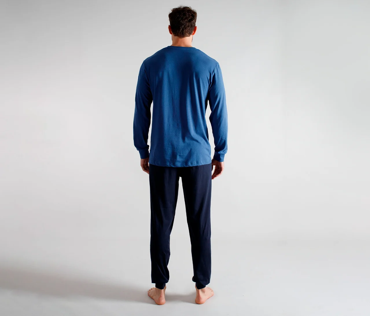 Homme de dos portant un t-shirt bleu à manches longues et un pantalon bleu foncé, pieds nus.